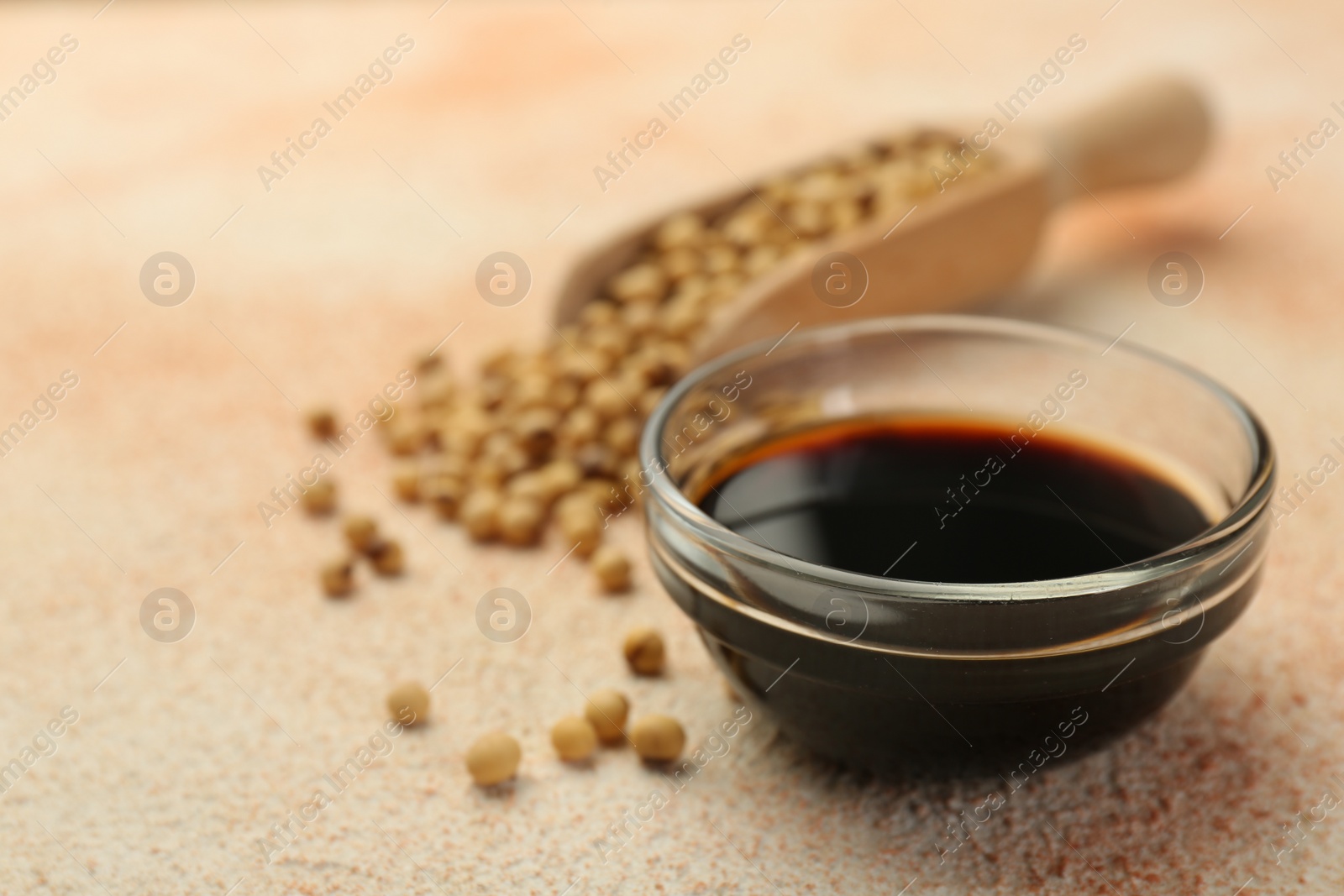 Photo of Soy sauce in bowl and beans on beige textured table, closeup. Space for text