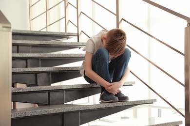 Sad little boy sitting on stairs indoors