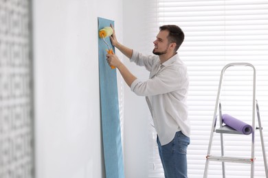 Man hanging light blue wallpaper in room