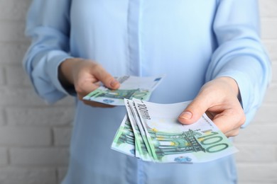 Photo of Woman holding 100 Euro banknotes near white brick wall, closeup. Money exchange