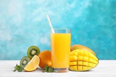 Photo of Glass with fresh mango juice and tasty fruits on wooden table