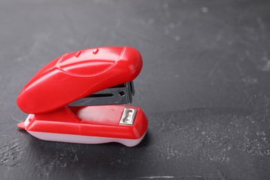 Photo of Red stapler on black textured table, space for text