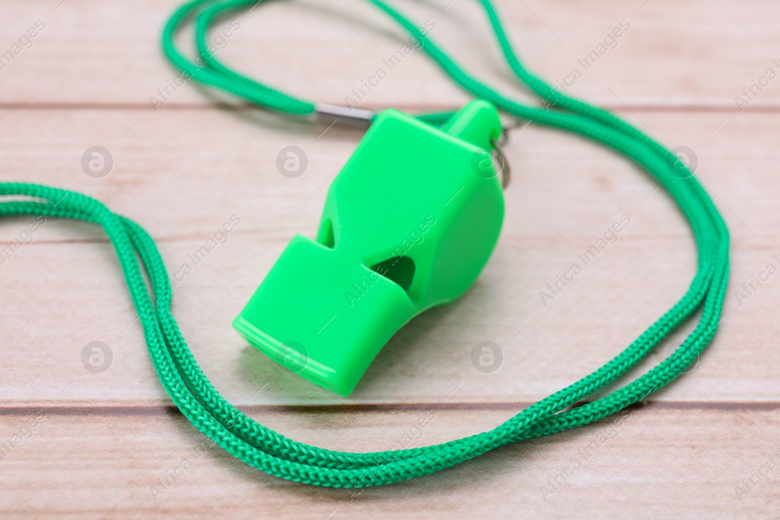 Photo of One green whistle with cord on light wooden table, closeup