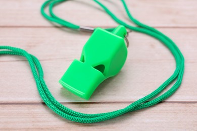 Photo of One green whistle with cord on light wooden table, closeup