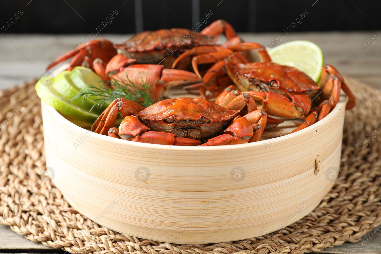 Photo of Delicious boiled crabs with lime and dill in bamboo steamer on table, closeup