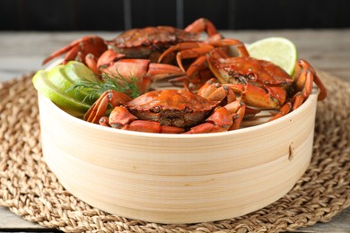 Photo of Delicious boiled crabs with lime and dill in bamboo steamer on table, closeup