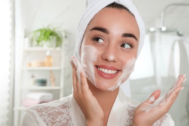 Photo of Beautiful young woman applying cleansing foam onto face in bathroom. Skin care cosmetic