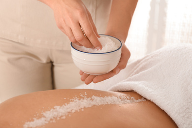 Young woman having body scrubbing procedure with sea salt in spa salon, closeup