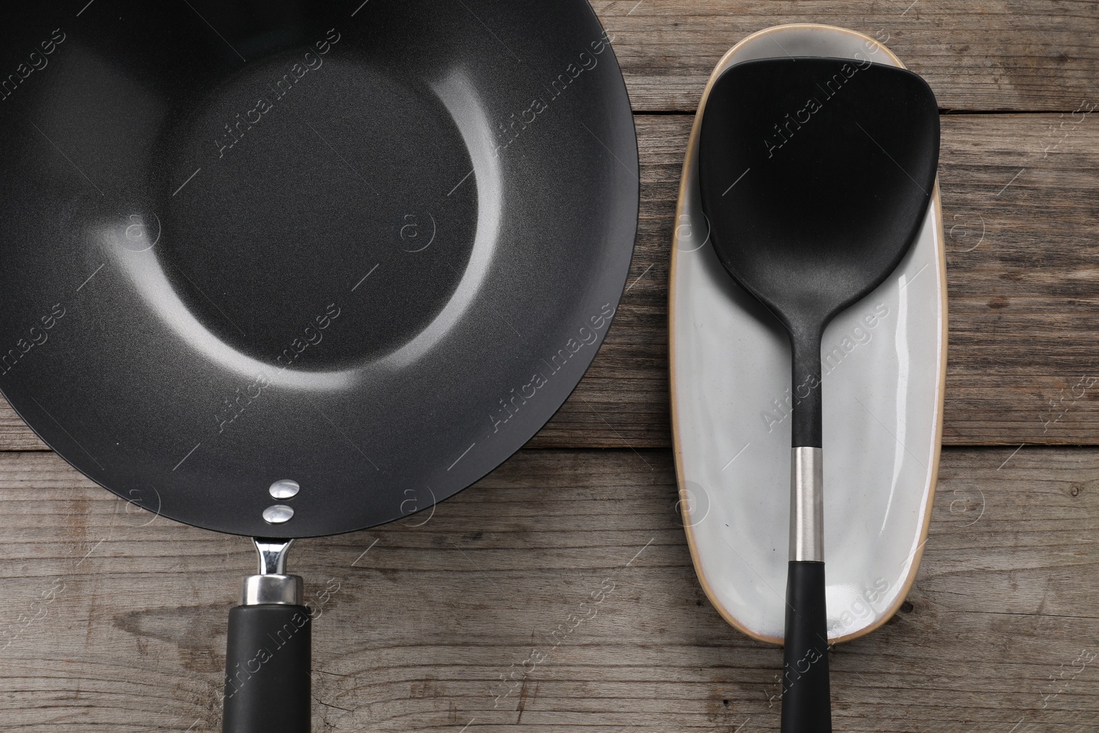 Photo of Black metal wok and spatula on wooden table, top view