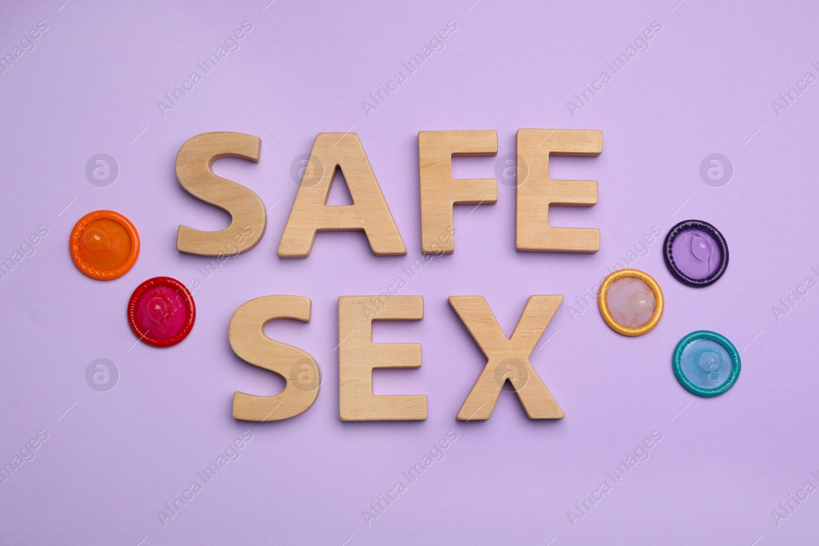 Photo of Flat lay composition with condoms and words SAFE SEX made with wooden letters on violet background
