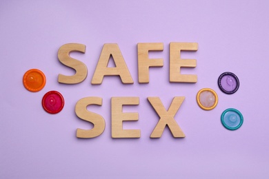 Flat lay composition with condoms and words SAFE SEX made with wooden letters on violet background