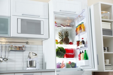 Photo of Open refrigerator full of products in stylish kitchen interior