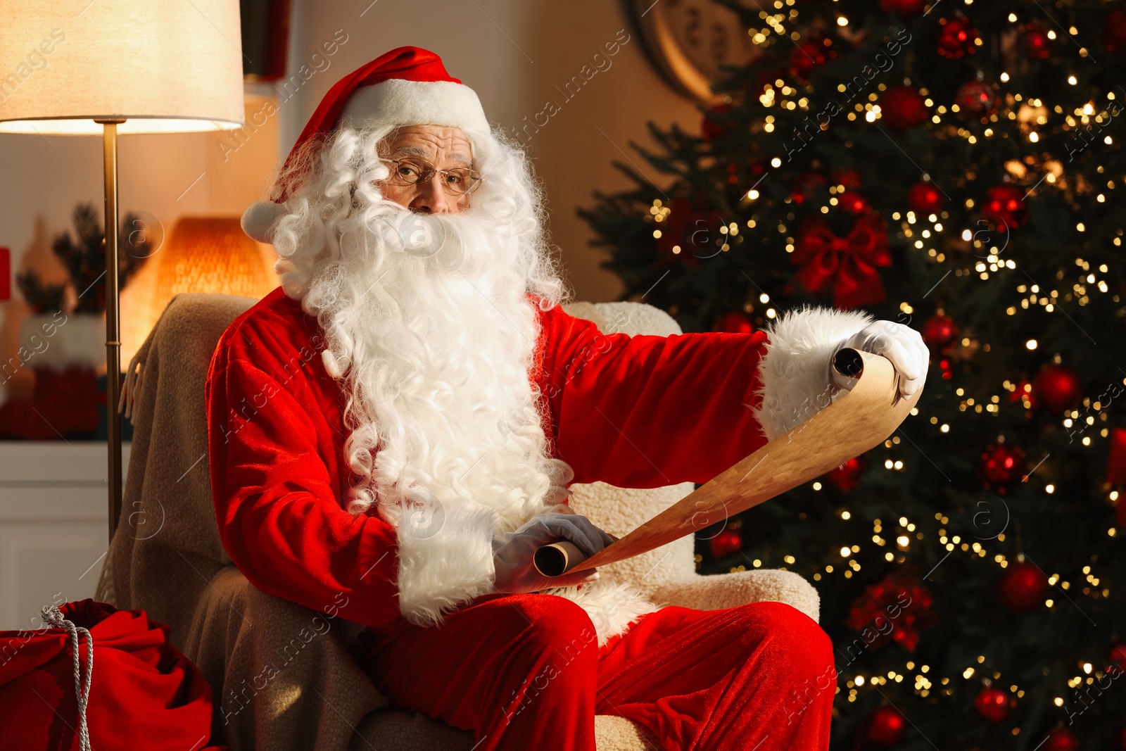 Photo of Santa Claus reading letter in room with Christmas tree