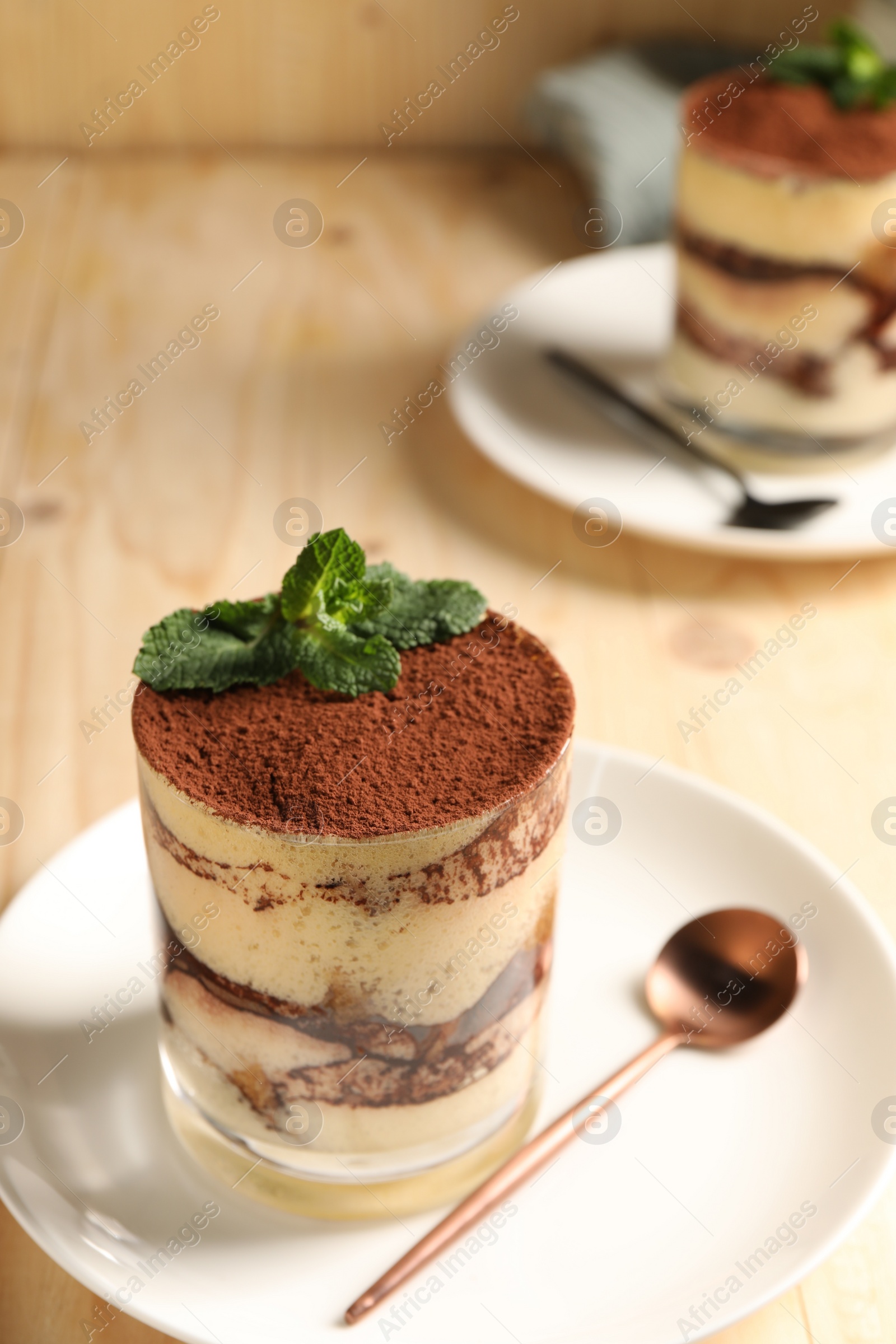 Photo of Tasty tiramisu and mint in glasses on light wooden table, closeup