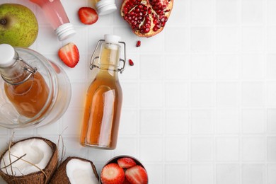 Photo of Tasty kombucha in glass bottles and fresh fruits on white tiled table, flat lay. Space for text