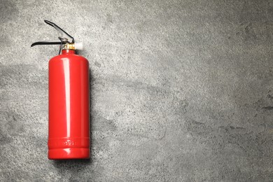 One red fire extinguisher on gray textured background, top view. Space for text