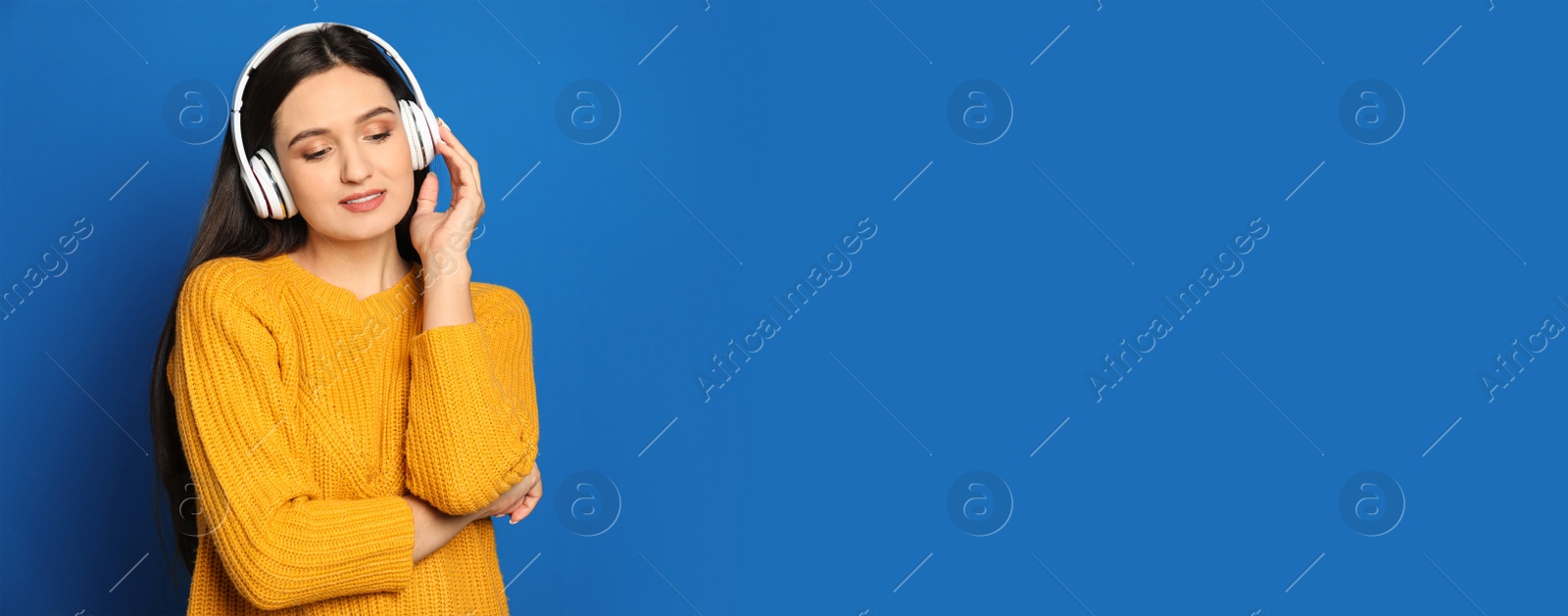 Image of Young woman listening to music with headphones on blue background, space for text. Banner design