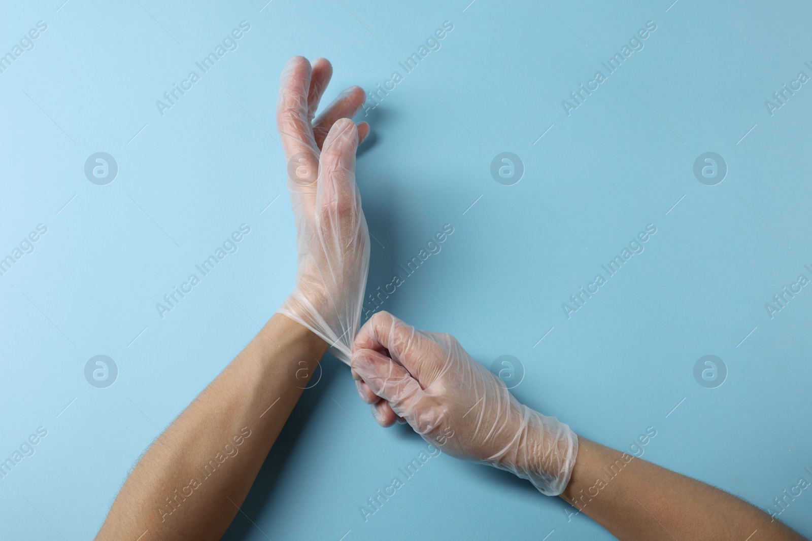Photo of Doctor wearing medical gloves on light blue background, top view