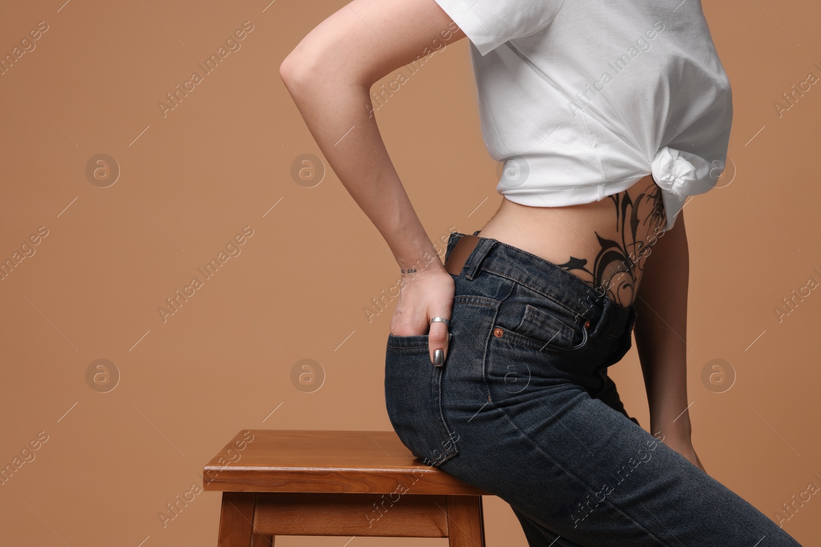 Photo of Woman with tattoo on belly sitting on stool against beige background, closeup