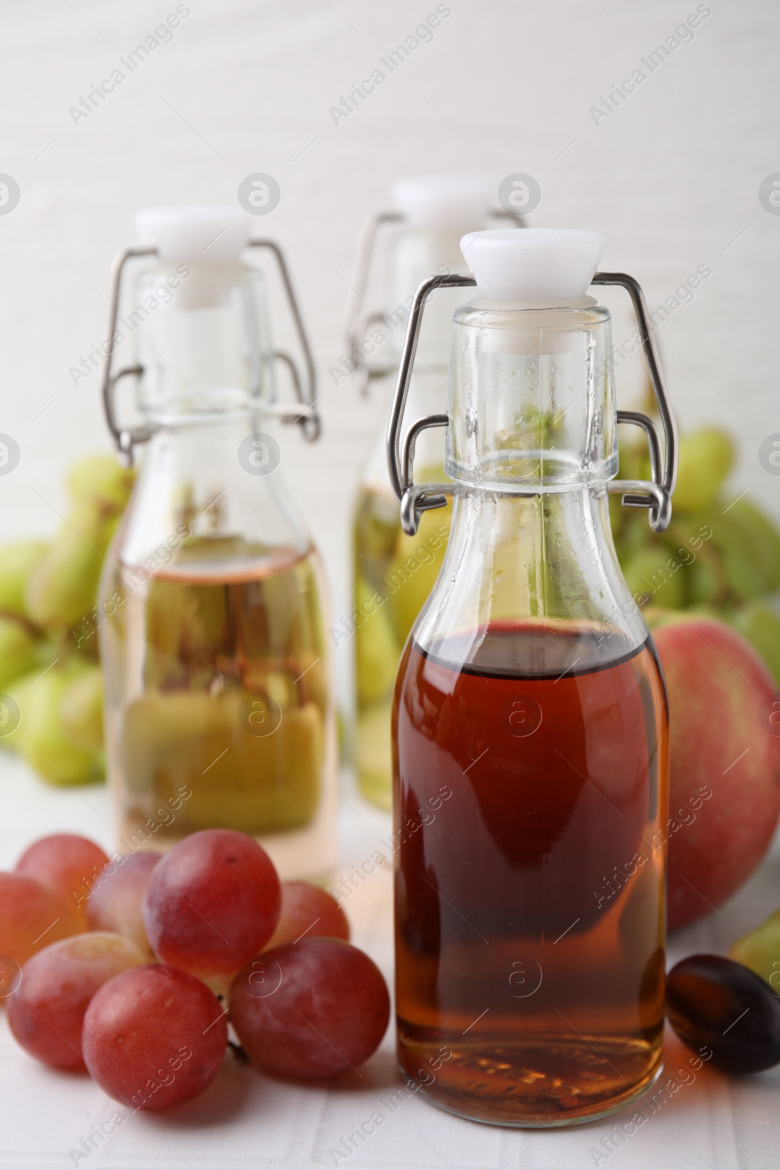 Photo of Different types of vinegar and ingredients on light tiled table, closeup