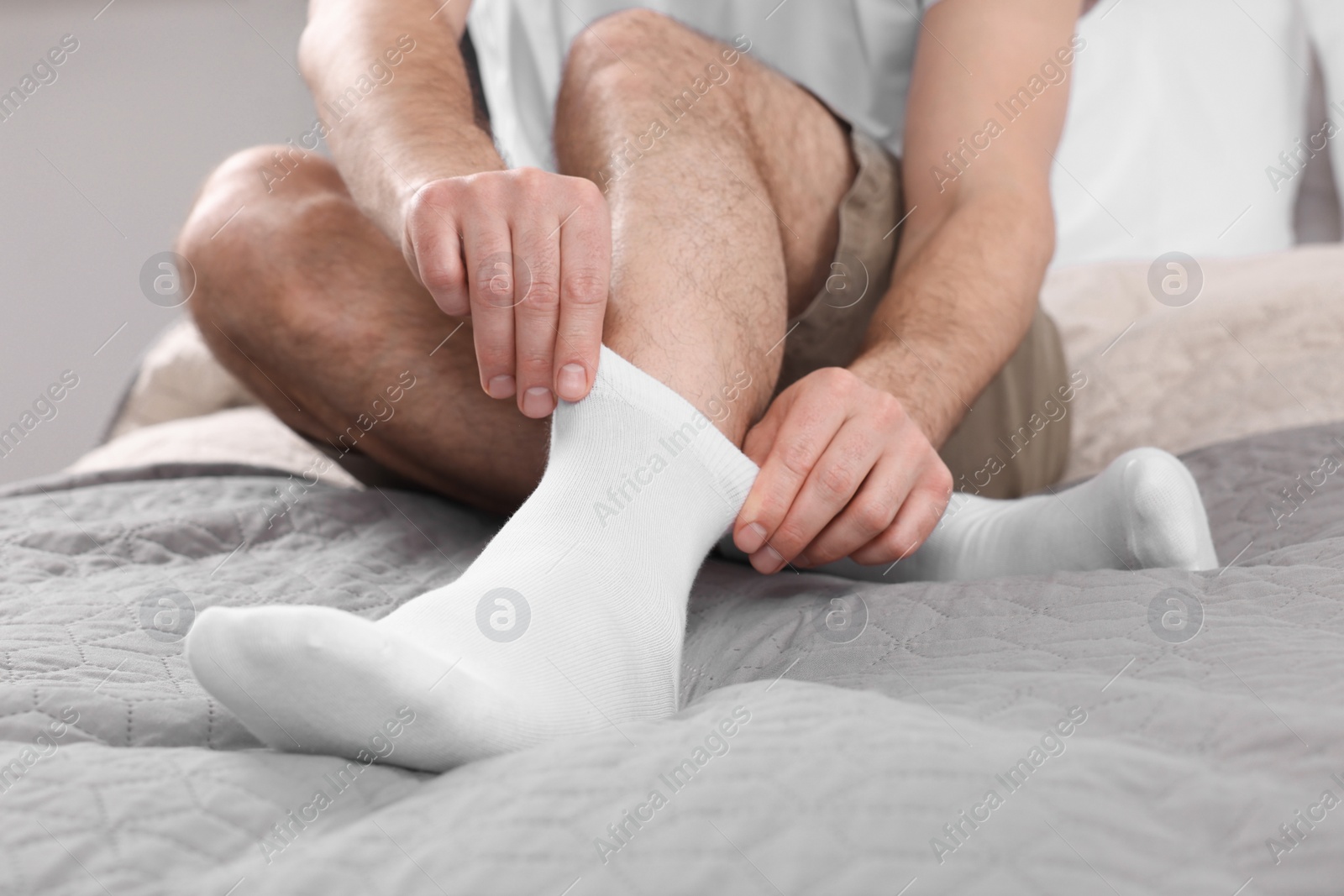 Photo of Man putting on white socks at home, closeup