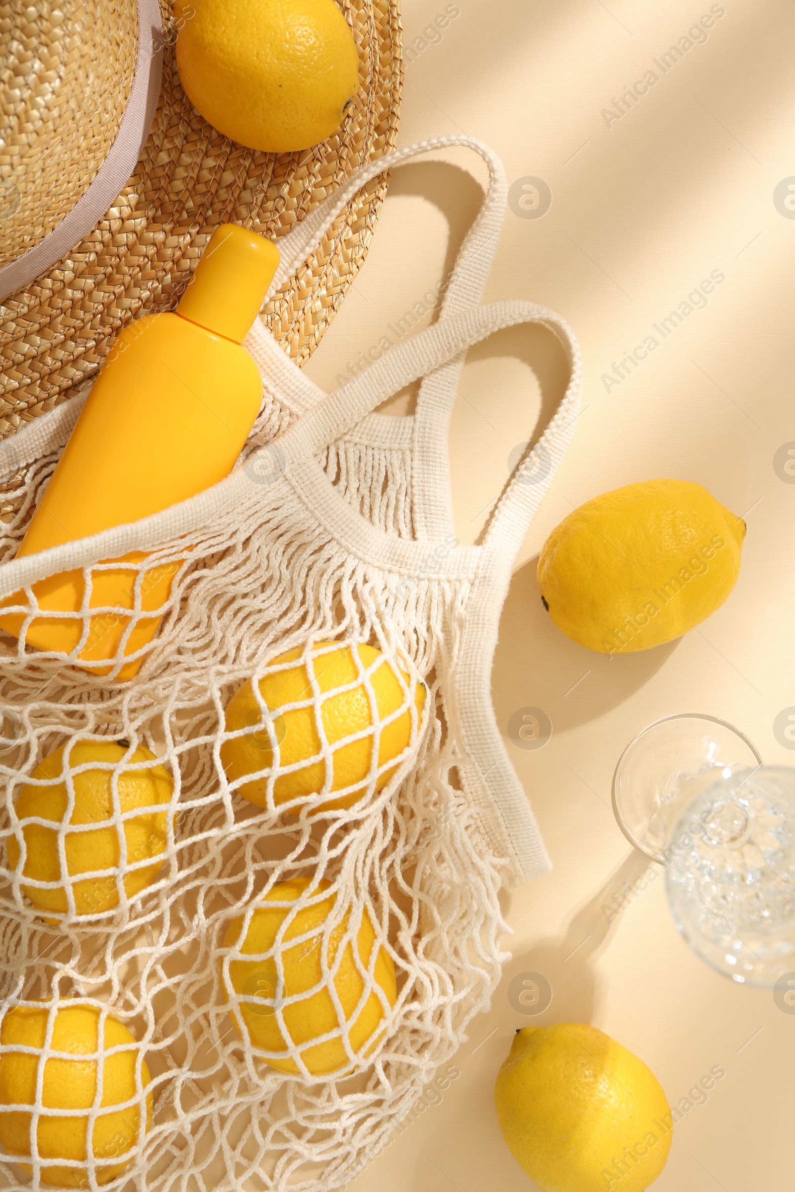 Photo of Fresh lemons, beach accessories in string bag and glass of drink on beige background, flat lay