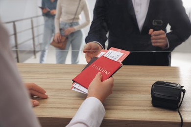 Photo of Agent giving passports with tickets to client at check-in desk in airport, closeup