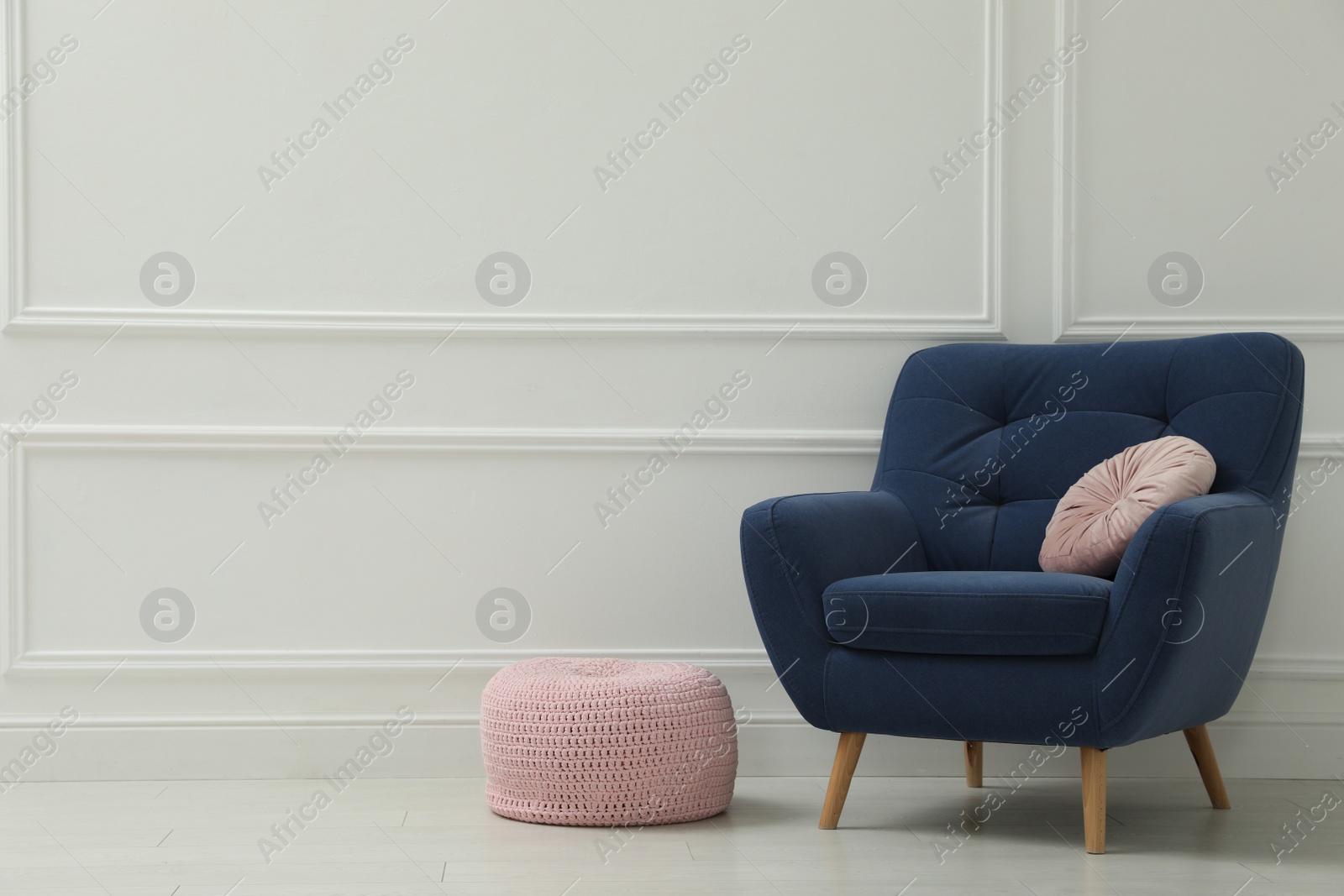 Photo of Knitted pouf and armchair with cushion near white wall indoors. Space for text