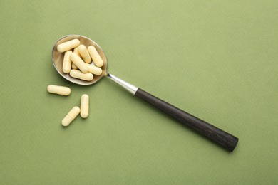 Photo of Vitamin capsules in spoon on olive background, top view