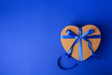Photo of Beautiful heart shaped gift box with bow on blue background, top view. Space for text