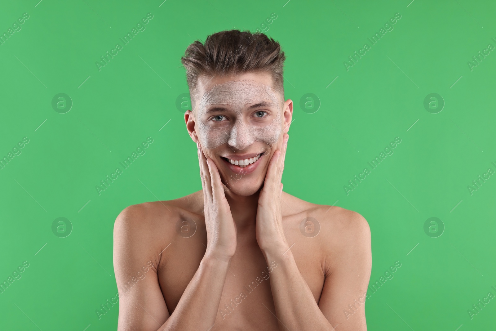 Photo of Handsome man applying facial mask onto his face on green background