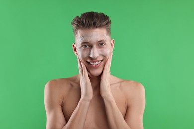 Handsome man applying facial mask onto his face on green background
