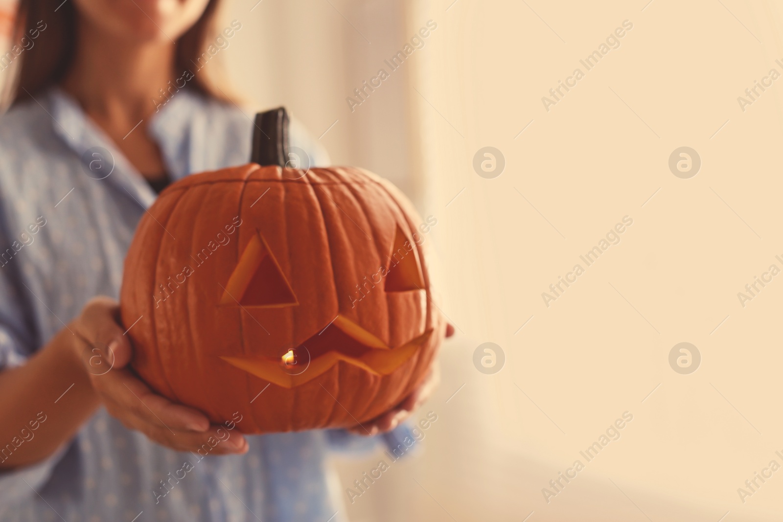 Photo of Woman holding pumpkin jack o'lantern indoors, closeup with space for text. Halloween celebration