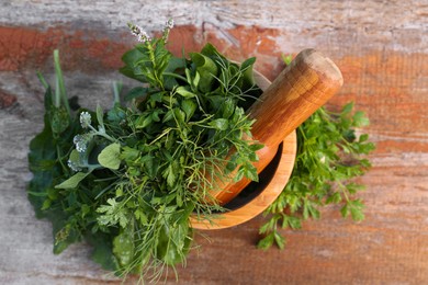 Photo of Mortar, pestle and different herbs on wooden table, top view
