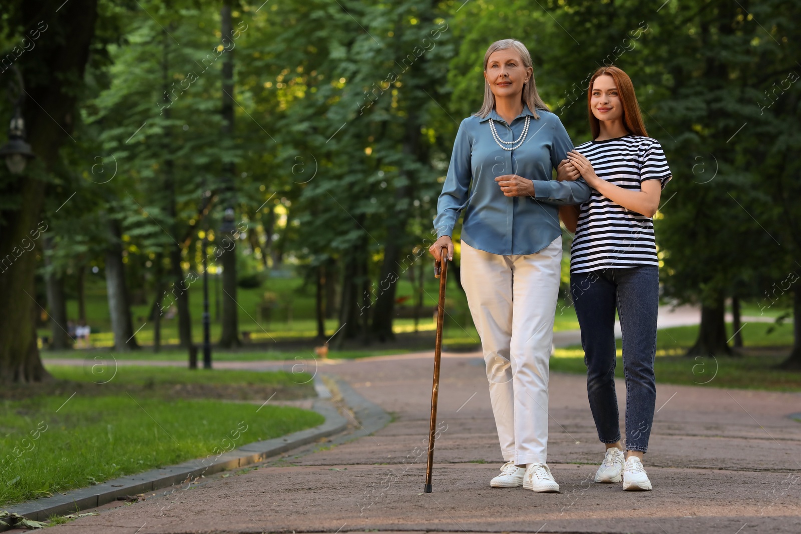 Photo of Senior lady with walking cane and young woman in park. Space for text