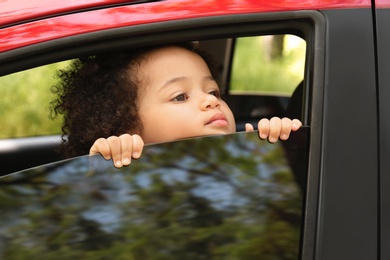 Photo of Little African-American girl alone inside car. Child in danger