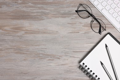 Photo of Home office. Computer keyboard, glasses and stationery on white wooden desk, flat lay. Space for text