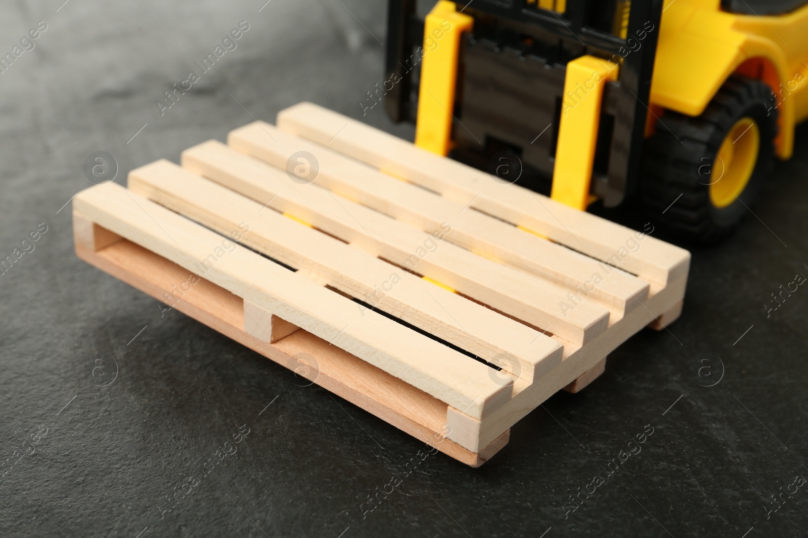 Photo of Toy forklift with wooden pallet on black table, closeup