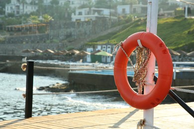 Orange lifebuoy hanging on post near sea, space for text