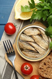 Photo of Tin can with tasty sprats served on blue wooden table, flat lay