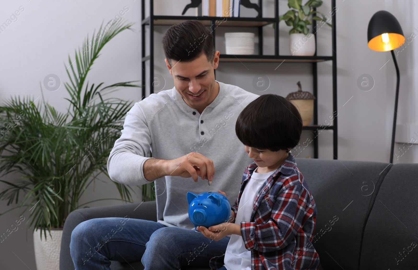 Photo of Little boy with his father putting coin into piggy bank at home