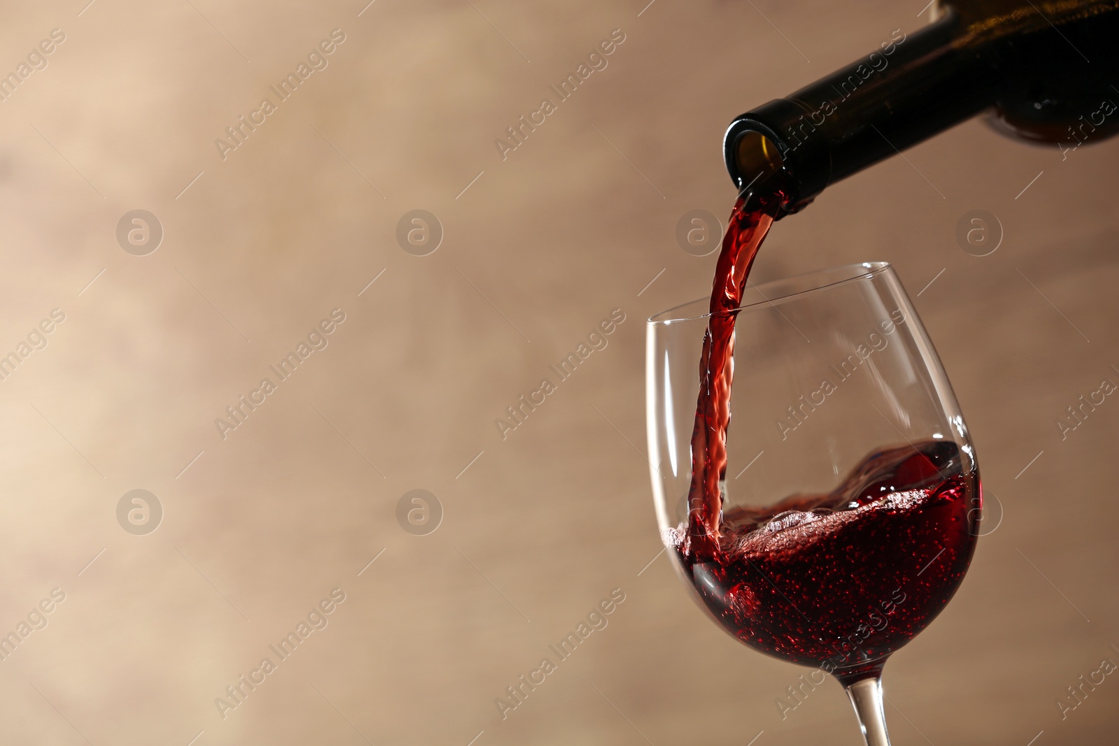 Photo of Pouring red wine into glass from bottle against blurred beige background, closeup. Space for text