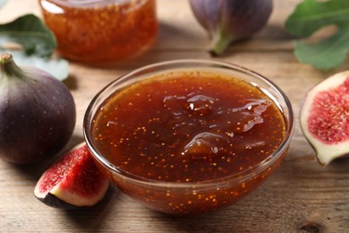 Bowl with tasty sweet jam and fresh figs on wooden table, closeup