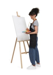 Photo of Young woman painting on easel with canvas against white background