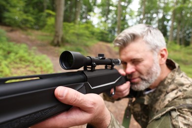 Man wearing camouflage and aiming with hunting rifle in forest, selective focus