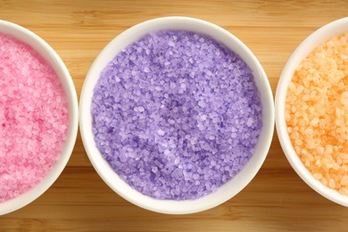 Bowls with colorful sea salt on wooden table, flat lay