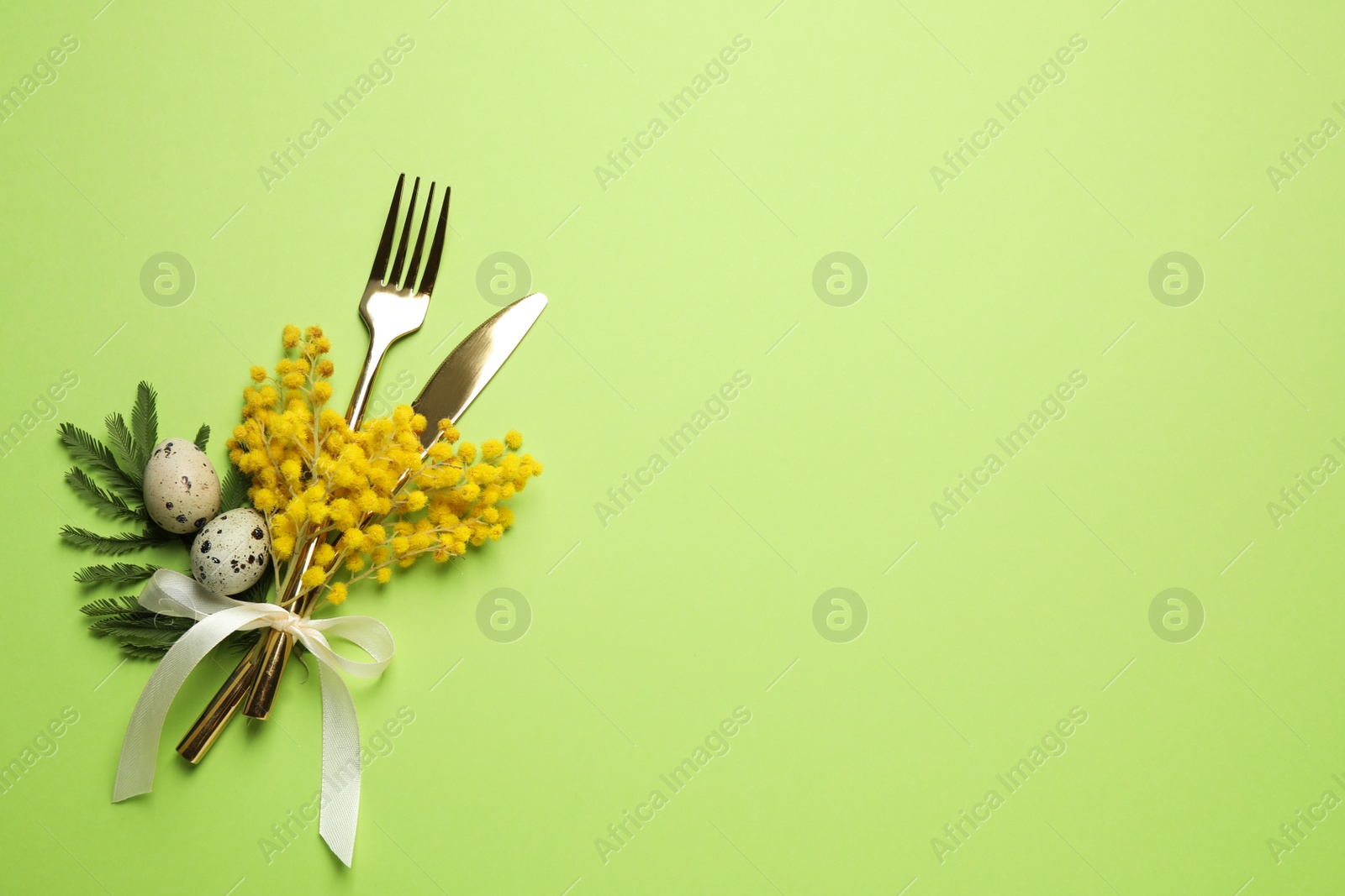 Photo of Top view of cutlery set with quail eggs and floral decor on green background, space for text. Easter celebration
