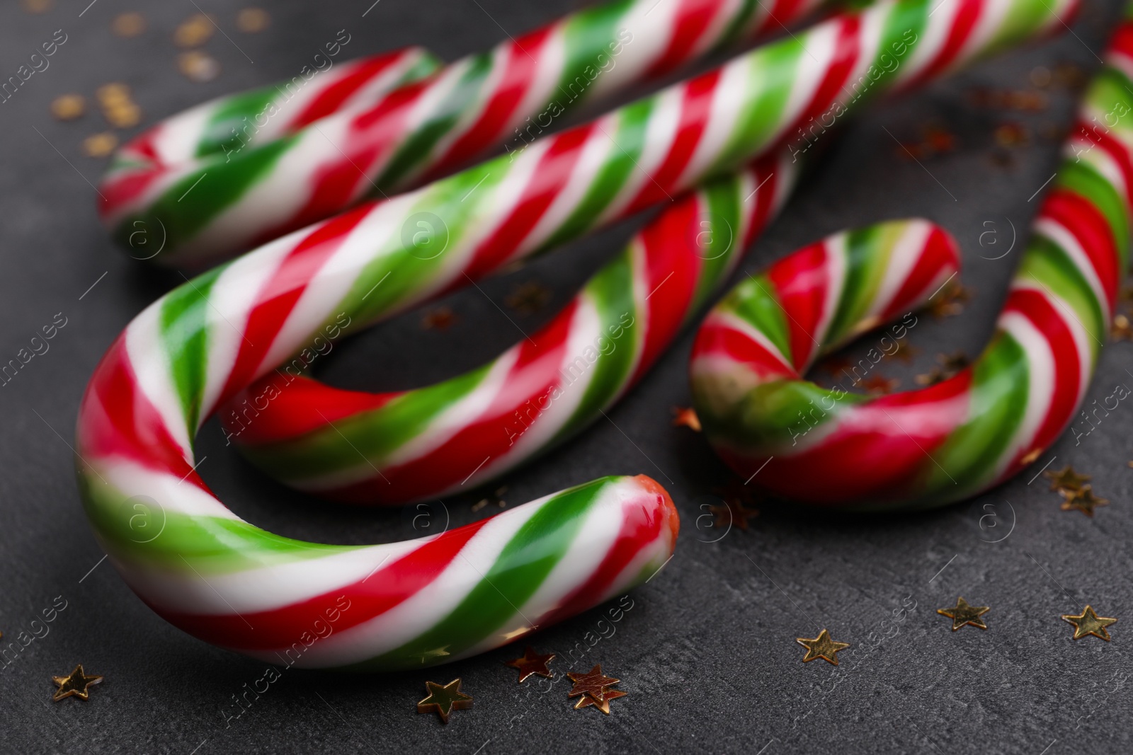 Photo of Many sweet Christmas candy canes and shiny confetti on grey background, closeup