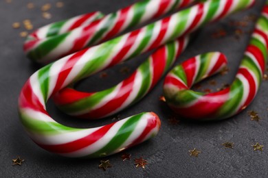 Photo of Many sweet Christmas candy canes and shiny confetti on grey background, closeup