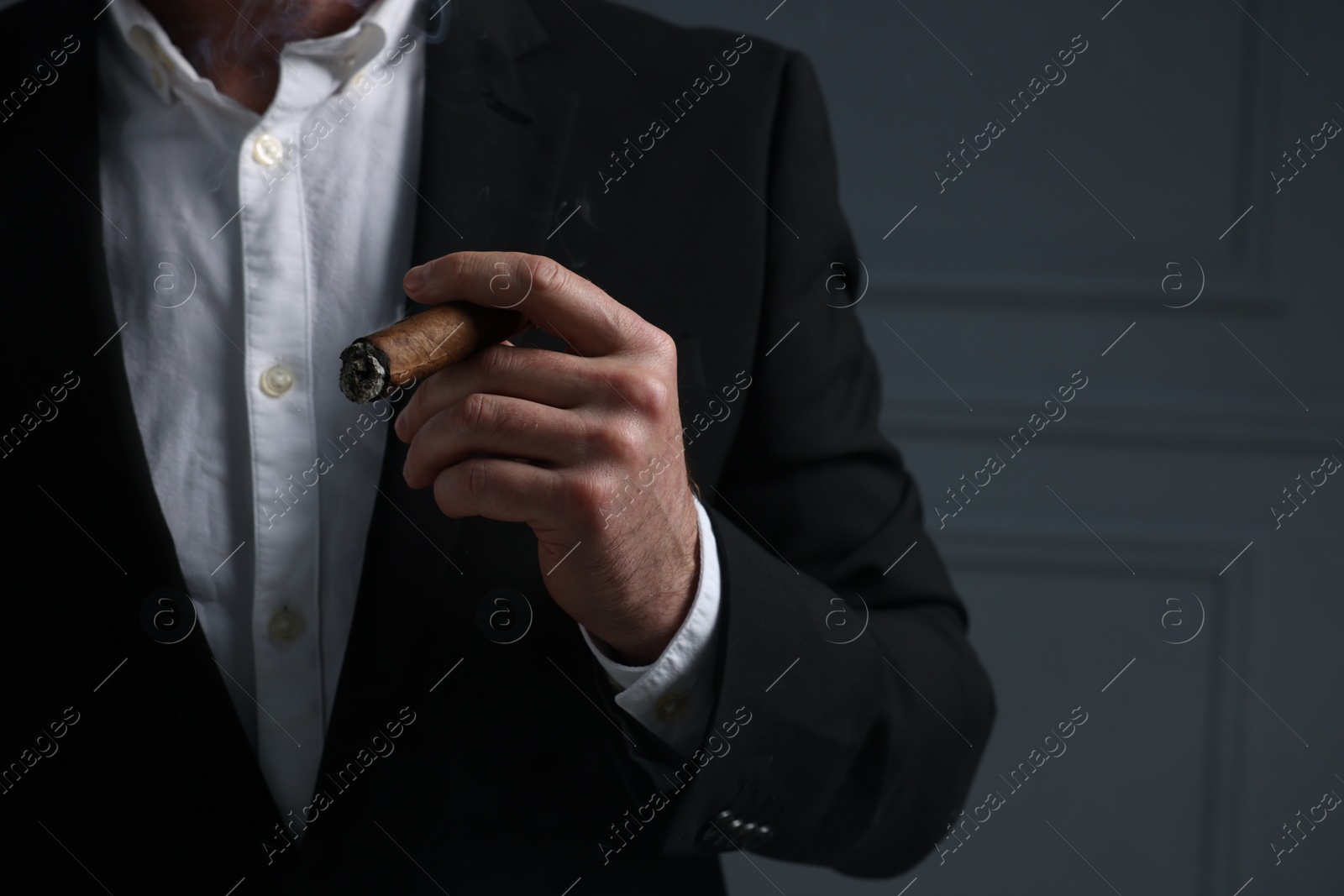 Photo of Man smoking cigar on dark grey background, closeup. Space for text